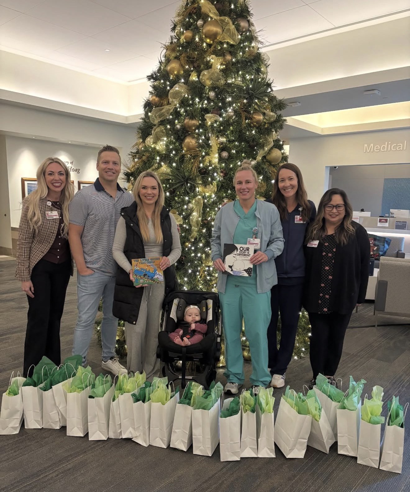 Our family with NICU nurses and care bags by the hospital Christmas tree